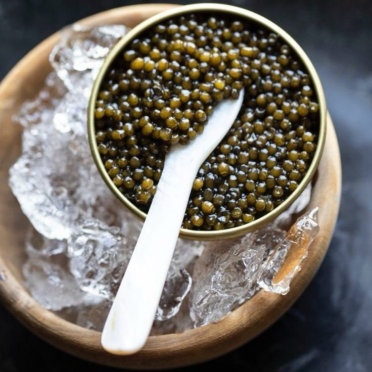 A mother-of-pearl Spoon in a tin of caviar served on ice.